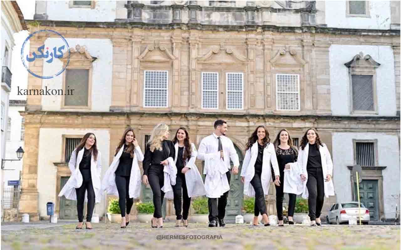 8 دانشجوی پزشکی خوشحال و شاد که لباس پزشکی بر تن دارند در حال قدم زدن جلوی یک ساختمان قدیمی. 7 دختر و 1 پسر. پسر به یکی از دخترها نگاه می‌کند. همه مشغول به تحصیل پزشکی در ترکیه به زبان انگلیسی هستند