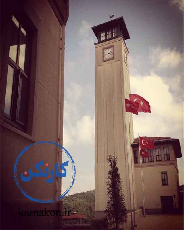 نشان و نماد دانشگاه کوچ برج ساعت  که در جلوی آن چند پرچم کشور ترکیه در باد برافراشته شده‌اند که می‌توانید در آن به تحصیل پزشکی به زبان انگلیسی در ترکیه بپردازید